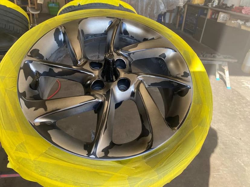 Alloy wheel masked with tape and freshly refinished in dark metallic during refurbishment